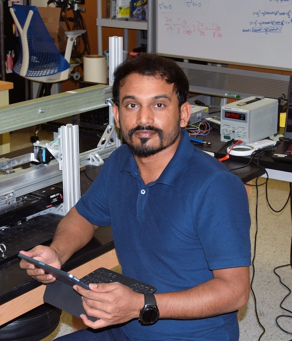 photograph of Bhart Meghwar with tablet in front of equipment with part of whiteboard in background